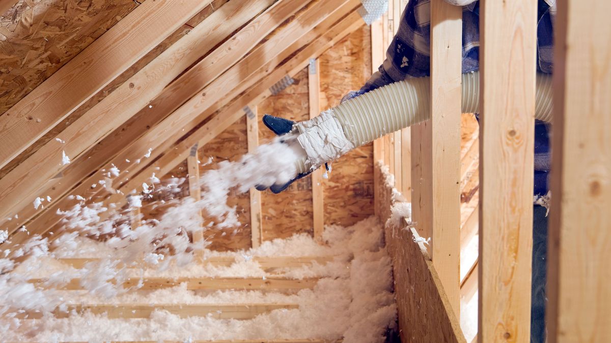 Worker Spraying Blown Fiberglass Insulation between Attic Trusses