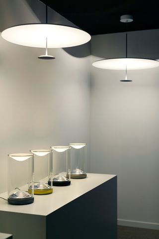 Four cylindrical lamps sit on a table with two large overhead lights