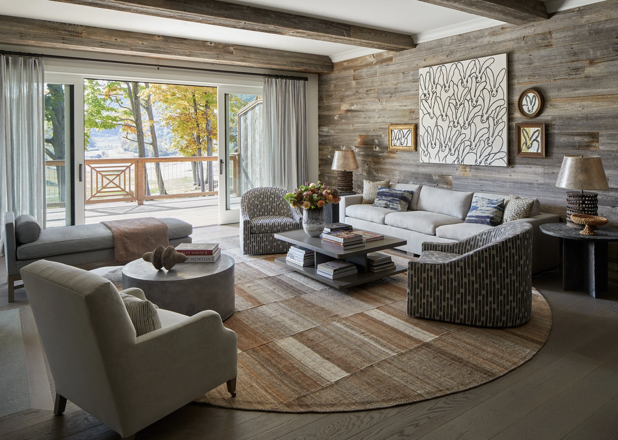 modern living room with timber panelling on the wall, large round tug, with gray armchairs, white sofa with patterned armchairs on either side and rectangular coffee table