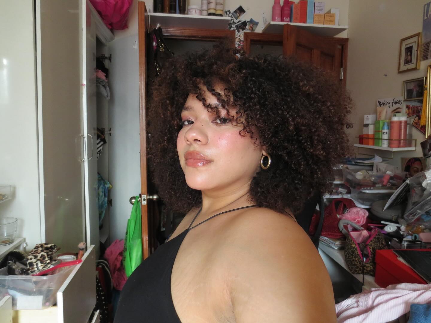 A woman with curly hair and layers taking a selfie in her bedroom