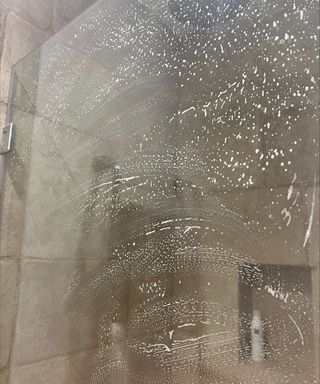 A foamy shower screen with brown tiles in the background