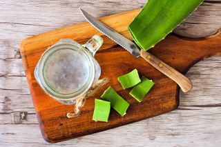 Collecting aloe vera juice on wooden chopping board with a knife and mason jar