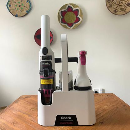 Shark Stainforce Spot Cleaner and caddy sitting on a wooden table in front of a white wall with colourful baskets on it