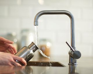 A woman washing a reusable bottle under a faucet