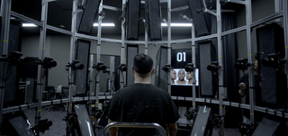 a man sits in a chair in a technological advancement while looking at a screen with a face on it in a still from eternal you