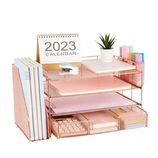 A rose gold desk organizer with papers in it