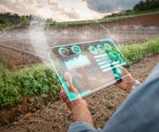 A farmer holds a futuristic tablet looking over a farm