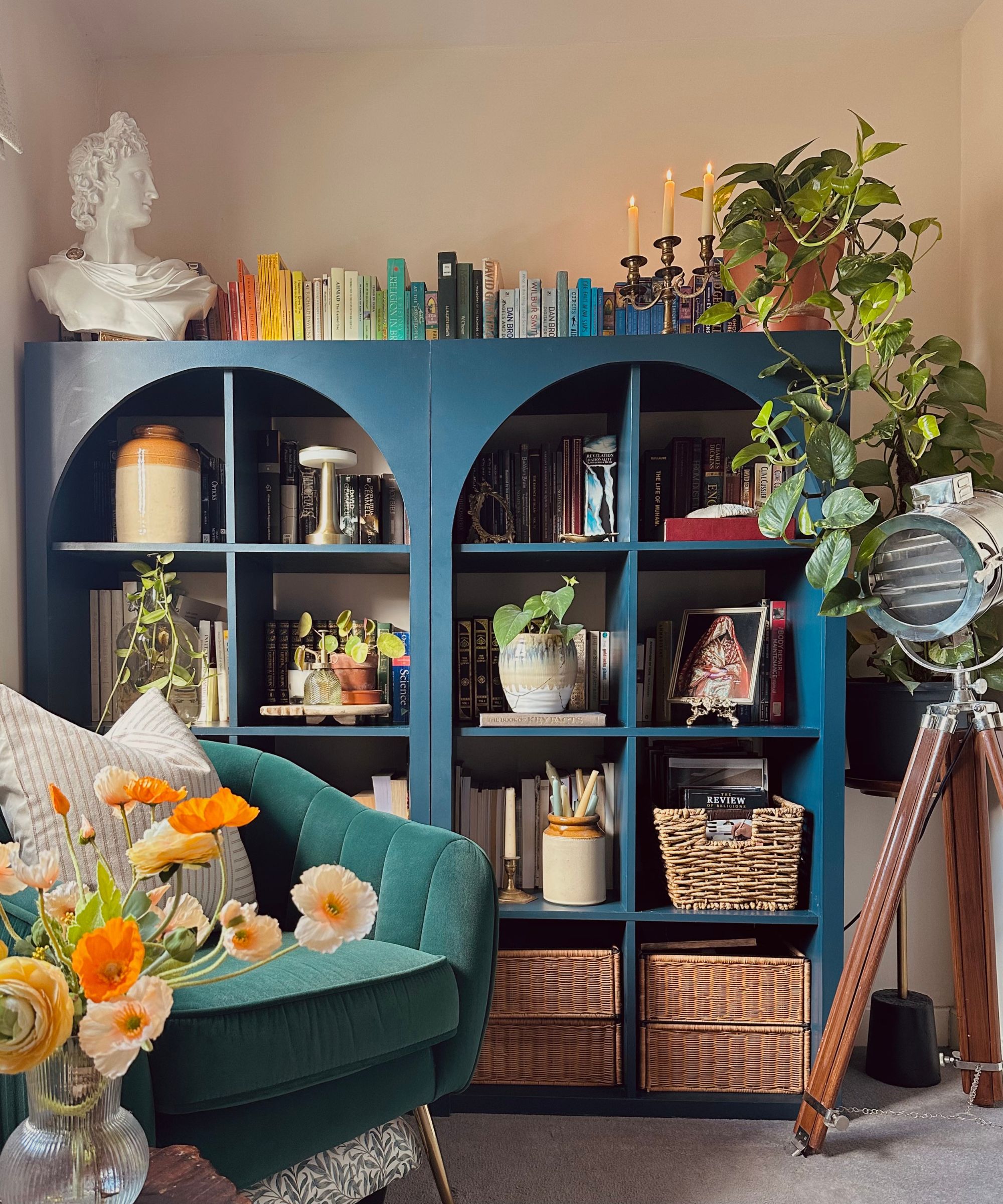 IKEA bookshelf painted navy with books and vintage decor, green velvet armchair and floor light