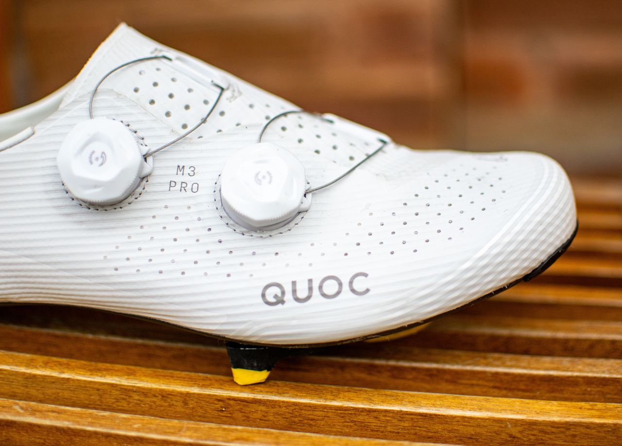 A white Quoc M3 Pro cycling shoe on a wooden chair