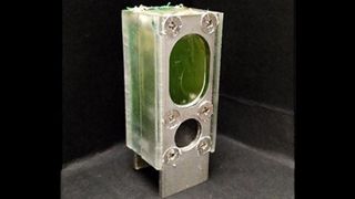 Algae battery viewed from side, clear plastic showing green water and girded by aluminum supports screwed in.