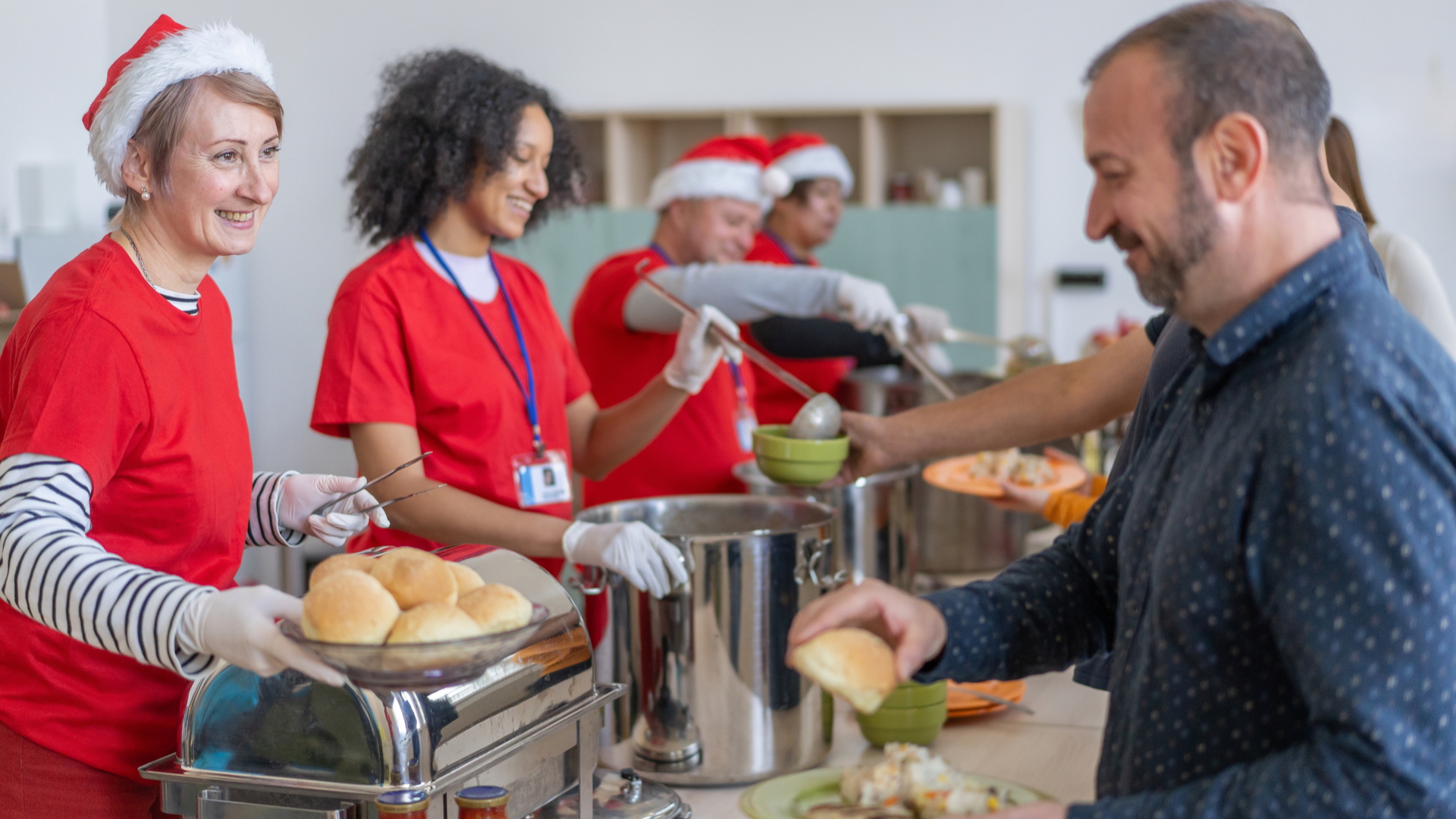 Soup kitchen volunteers serving food at Christmas, wearing Santa hats