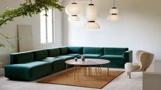 modern living room with long teal green sectional sofa in L shape with small orange rug, pinwheel coffee table, sherpa armchair, and three paper pendant lights hanging overhead