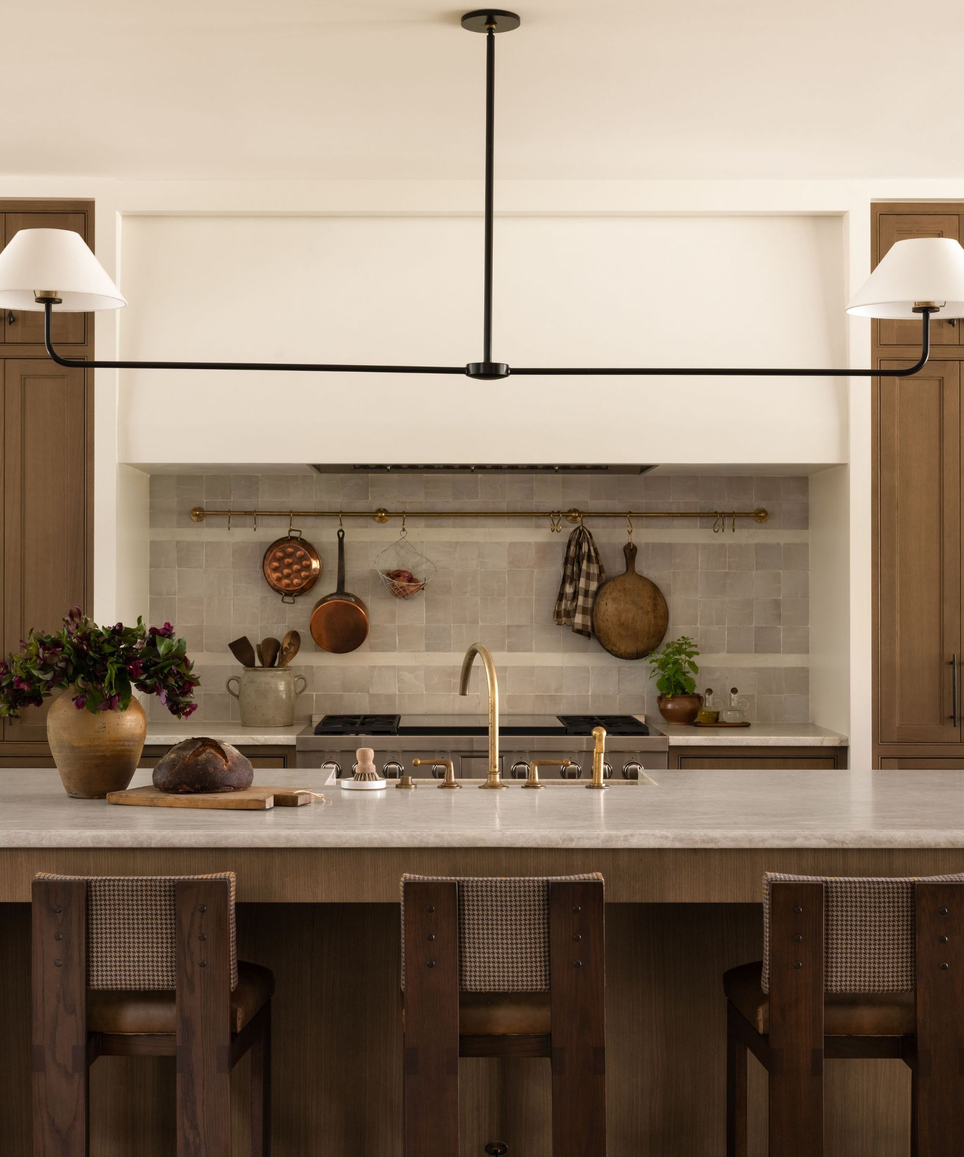 A kitchen with wooden cabinets, white walls, a white range hood, and a natural stone backsplash