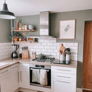 Calm small kitchen with sage green walls, white metro backsplash, and floating shelves with glass storage jars and kitchen bits in mint hues