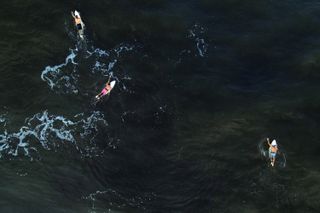 An aerial view showing three surfers wading into the ocean at Playa El Zonte in El Salvador