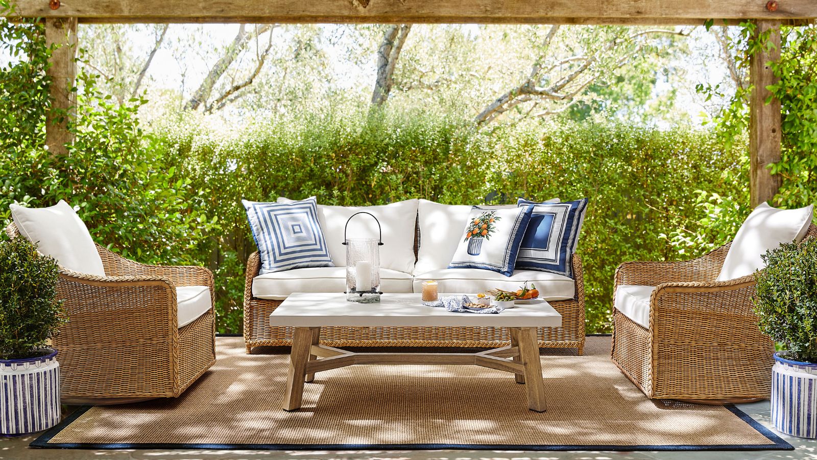 Outdoor patio area with a pergola and wicker furniture sofa and armchairs styled with blue and white cushions with orange motifs