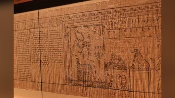 7. This image shows a part of the Book of the Dead. On the left is a block of hieratic text. On the right is an image of Osiris, the ancient Egyptian god of the underworld, sitting on a throne whilst wearing a crown with offerings before him.