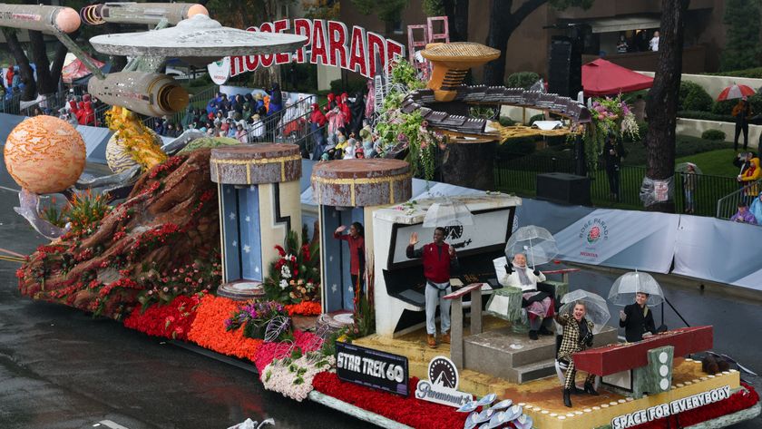 A parade float with the saucer spaceship from the hit show Star Trek with people sitting with clear umbrellas at the front of the float. 