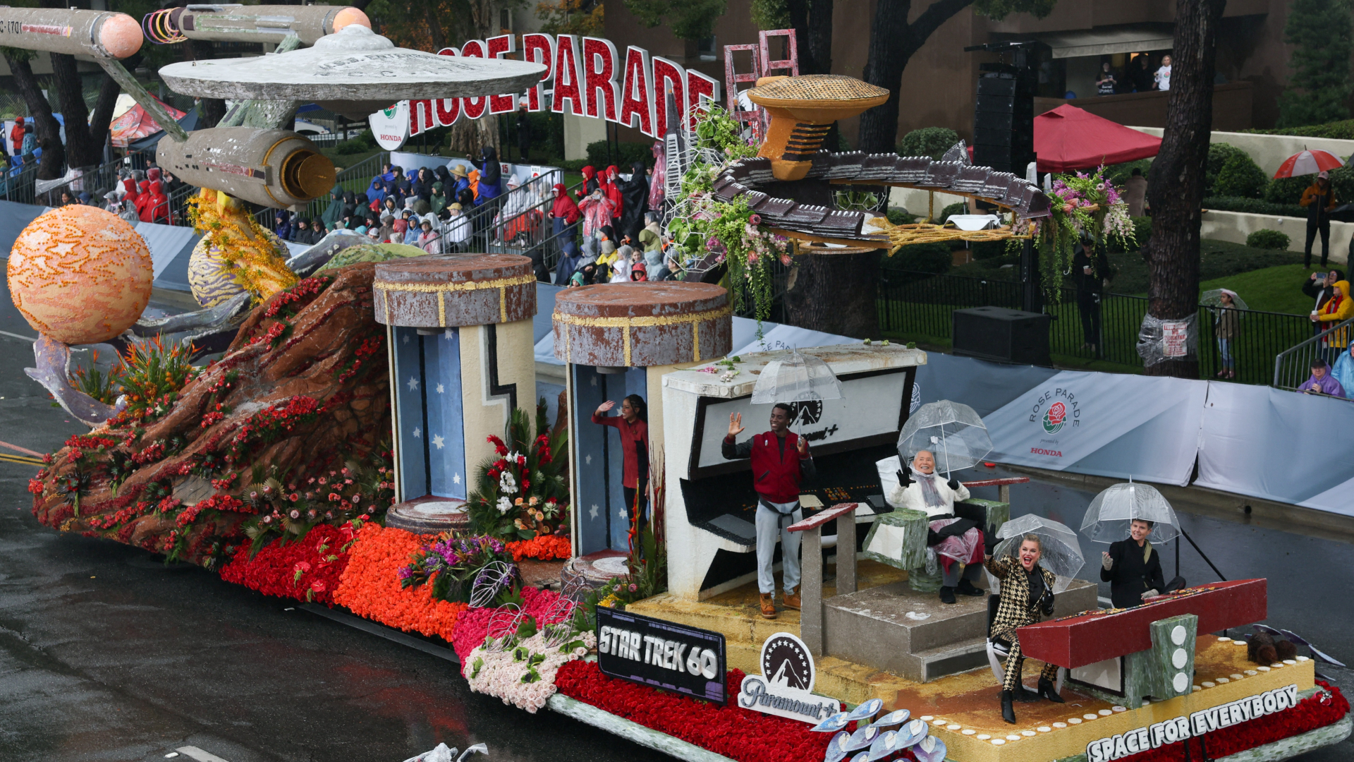 A parade float with the saucer spaceship from the hit show Star Trek with people sitting with clear umbrellas at the front of the float.