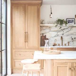 blonde wood kitchen with full height pantry cupboard and island and marble splashback and worktop