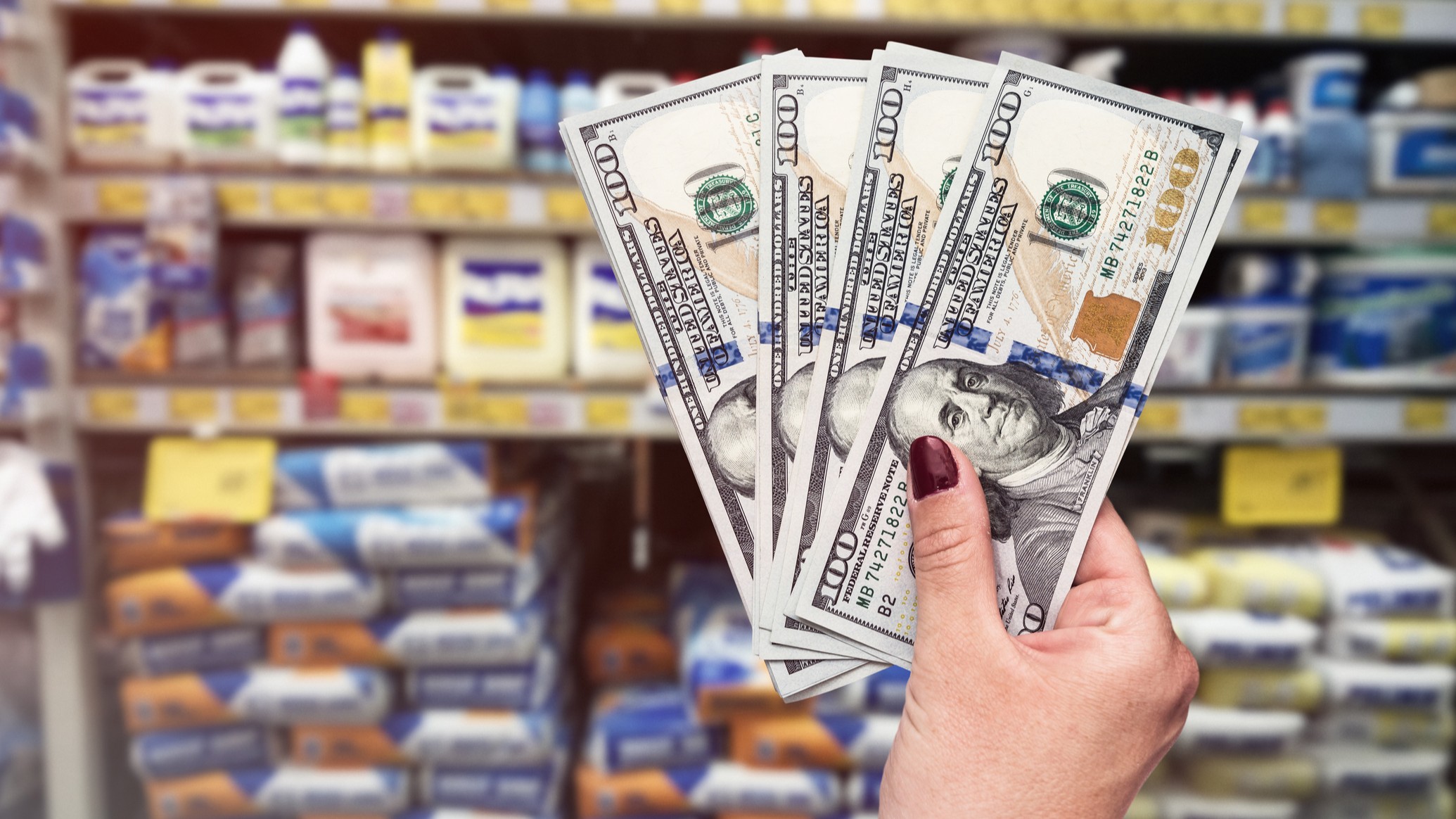 A hand holds a few $100 bills in a shopping aisle.
