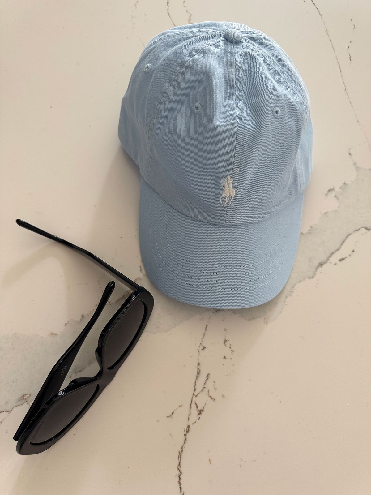 Light blue Polo hat on a table next to black sunglasses.