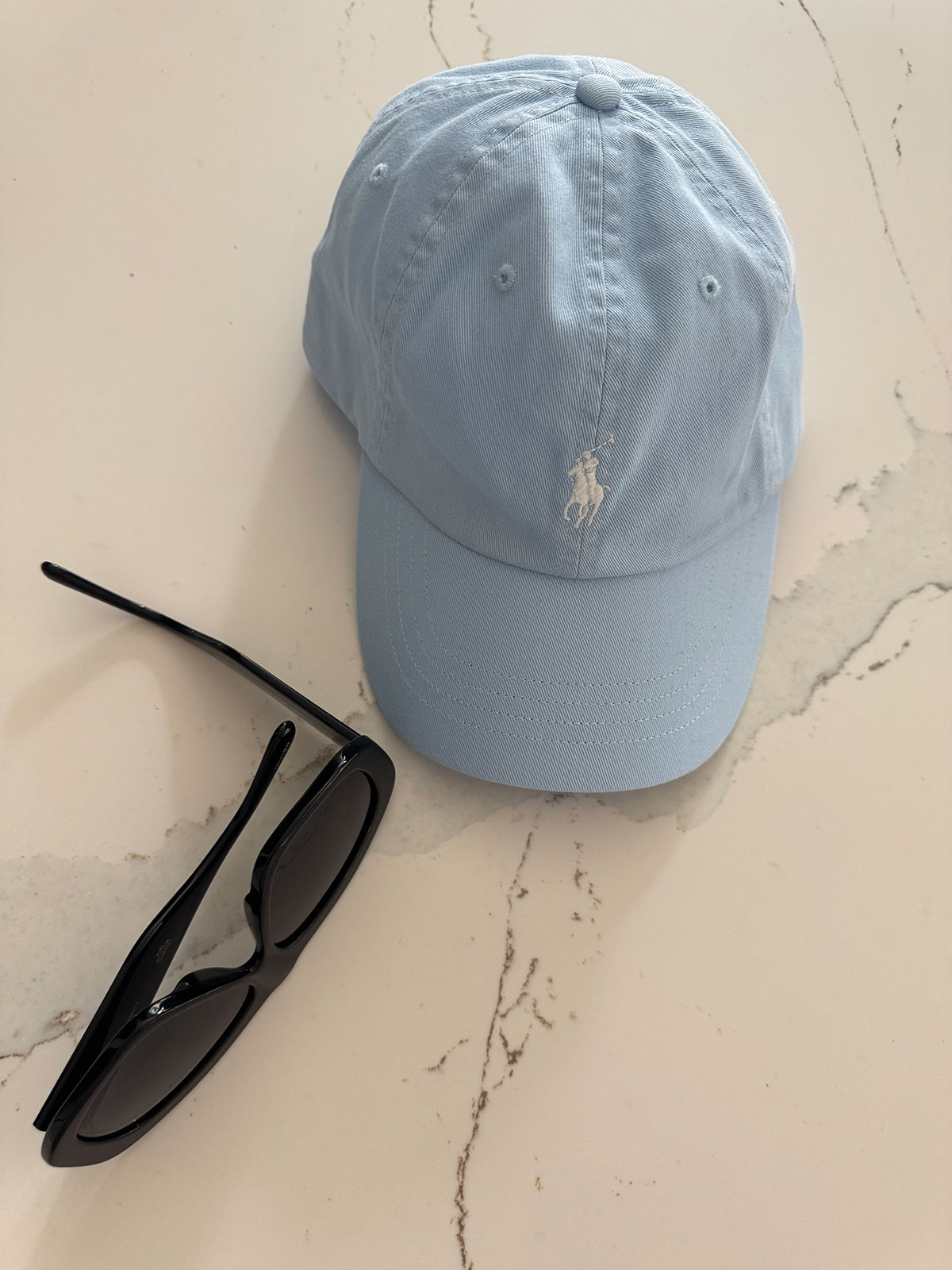 Light blue Polo hat on a table next to black sunglasses.