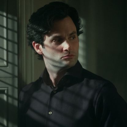 penn badgley as joe goldberg standing in a dark room in you season 5