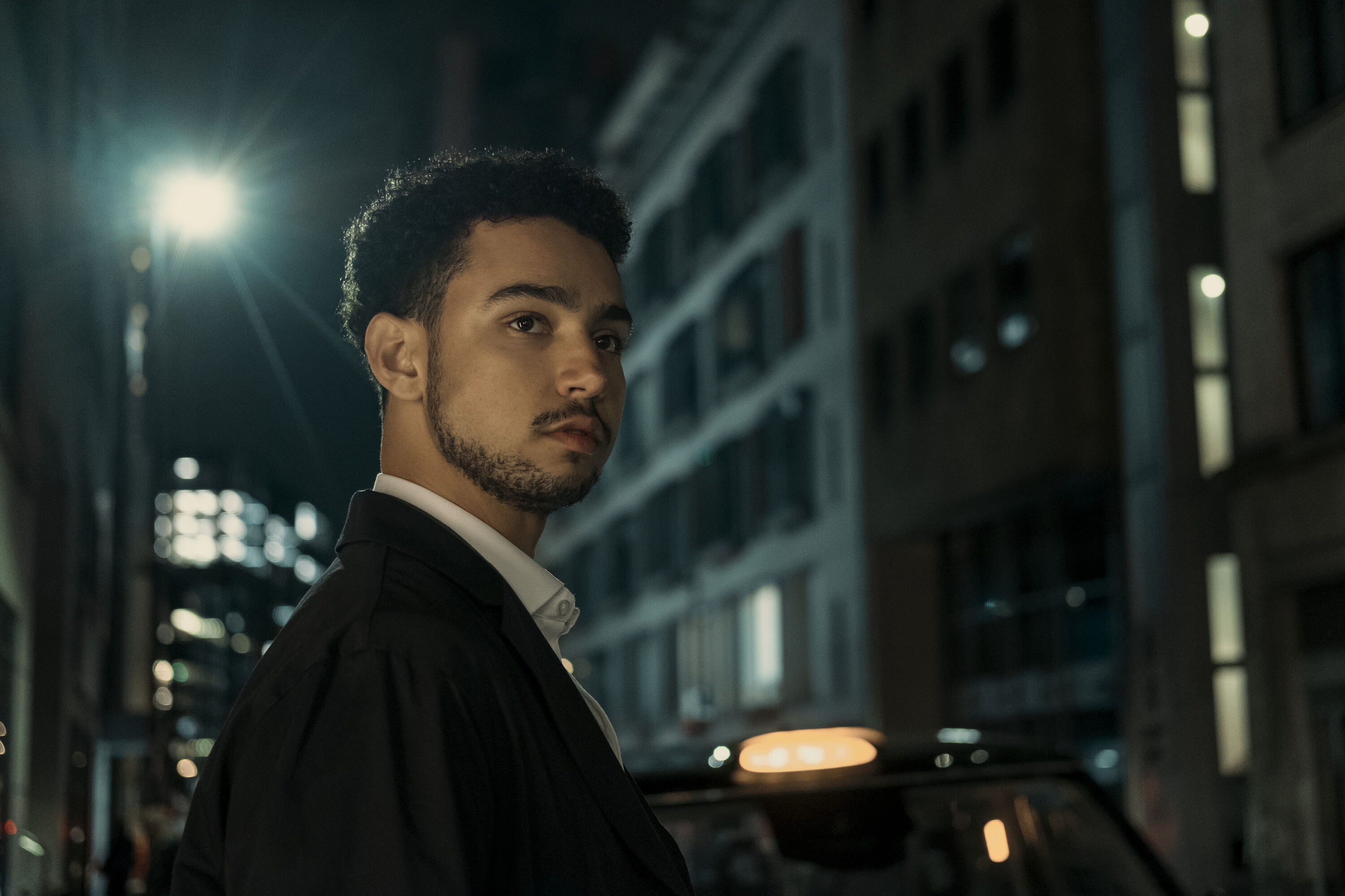 archie madekwe as luke wearing a suit standing in a dark london street at night in steal