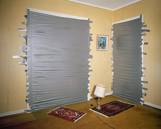 A room with two doorways cover by silver duck tape, two red patterned rugs and a lamp.