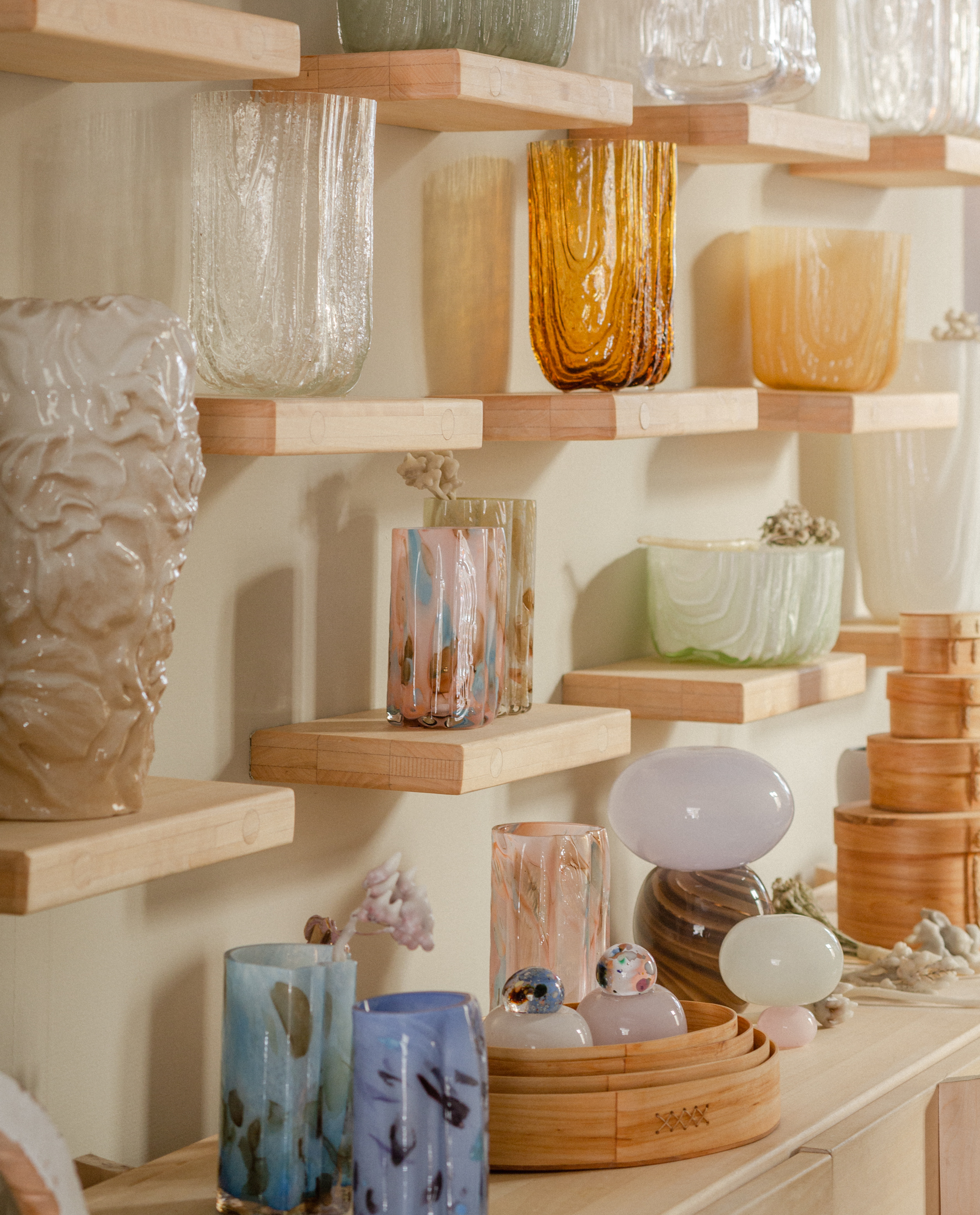 A whimsical series of sculptures with an organic silhouette and pastel shaded colors sit in a salmon-tinted gallery room on top of a wood and marble-topped table.