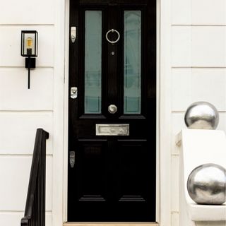 front door colour ideas, house with black front door, white painted exterior walls, silver hardware, railings, step up, wall light