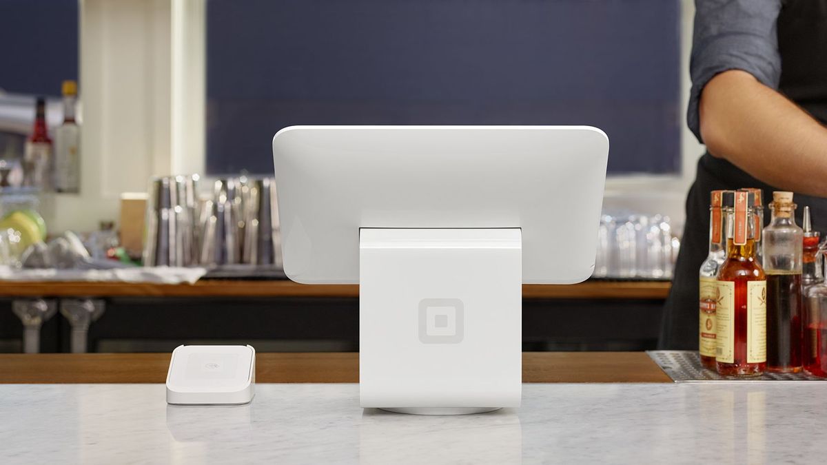 A white Square stand sits on a bar counter, with a Square payment machine next to it