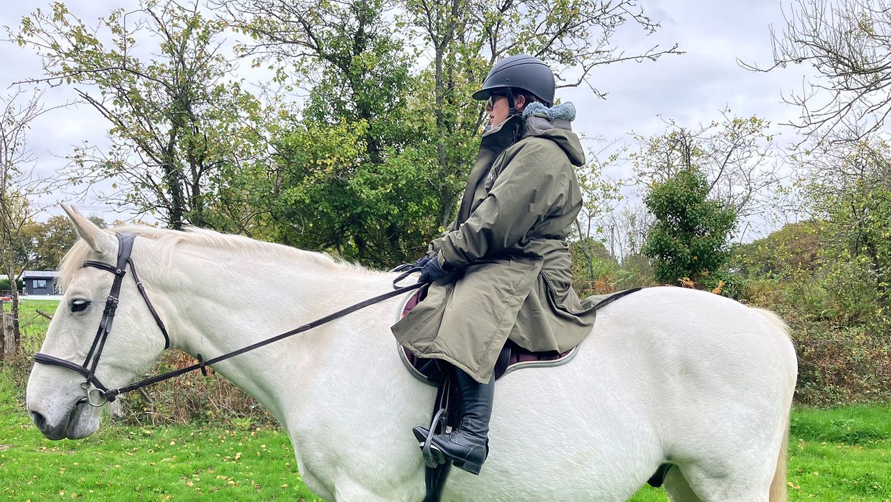Rider wears Reincoat Pro Robe on a horse, viewed from the side