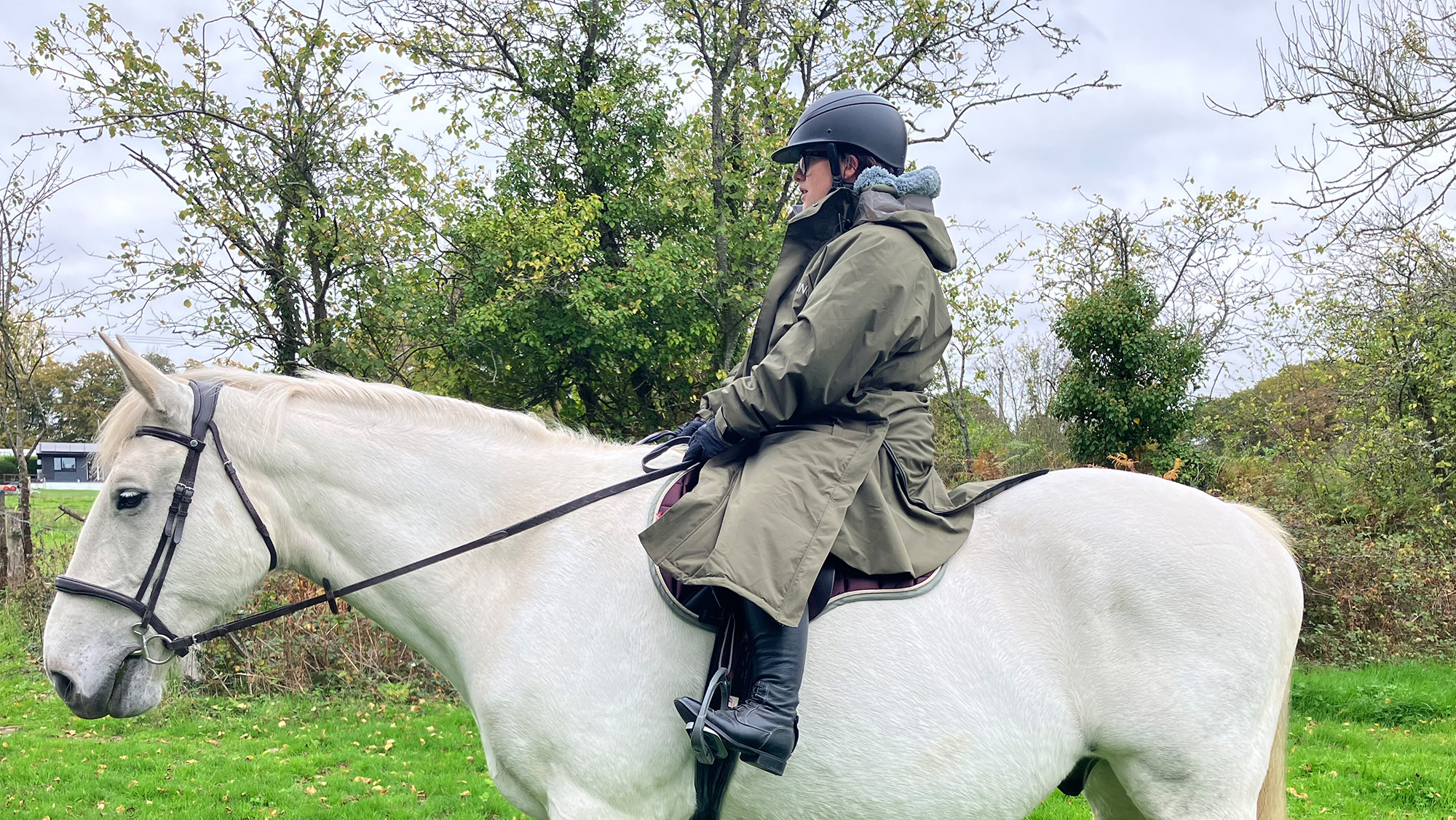 Rider wears Reincoat Pro Robe on a horse, viewed from the side