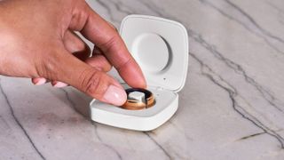 The Evie smart ring in its charging case, with a woman's hand reaching to pick it up. 