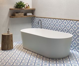 blue and white geometric tiles on floor and lower section of wall in bathroom with white freestanding bath
