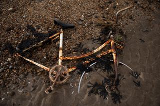 Corroded bike with wheels missing is half buried in mud