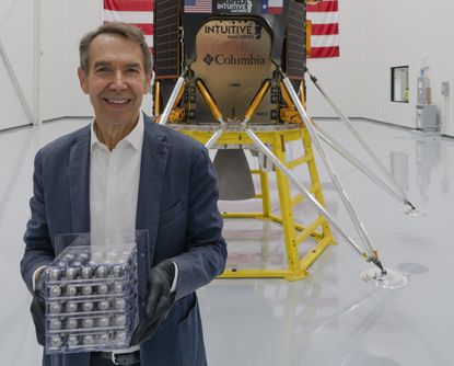 Jeff Koons in front of Intuitive Machines lunar module, holding his Jeff Koons: Moon Phases sculptures in a clear cubed case