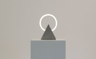 The circular neon light is set on a triangle stand.