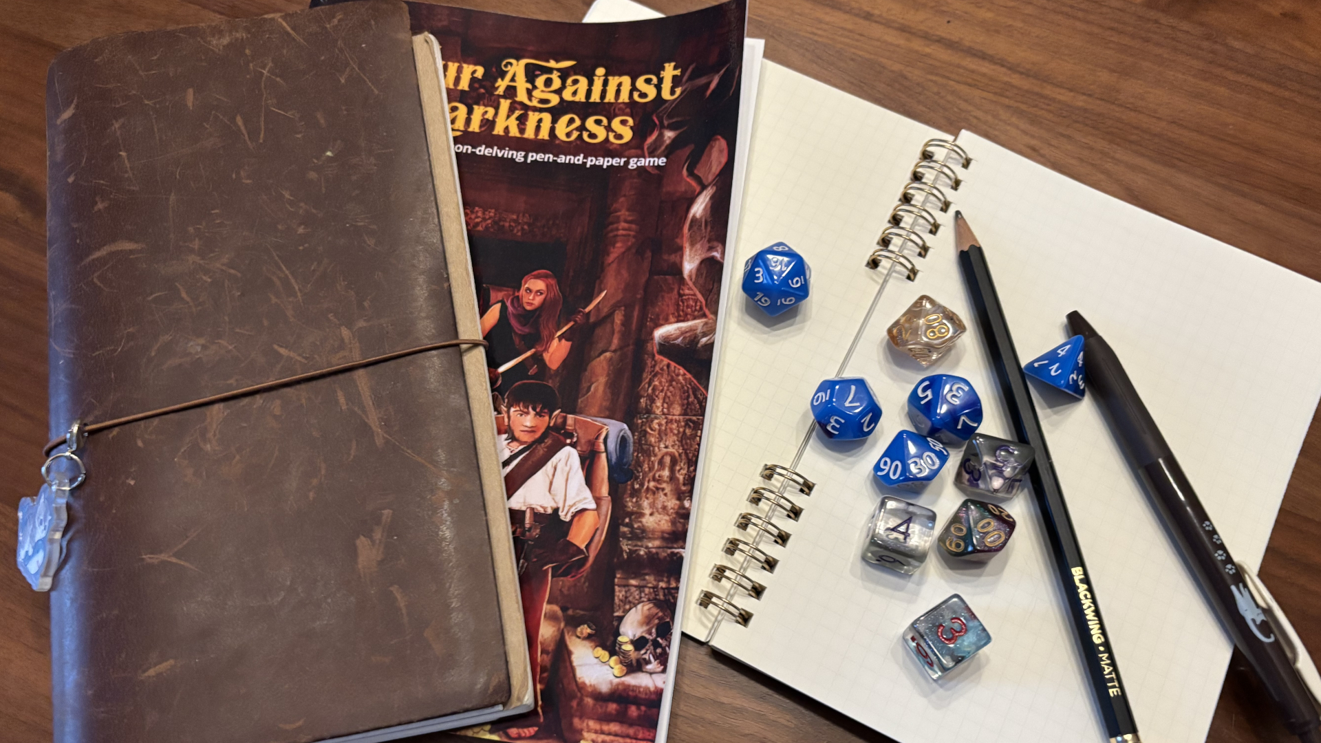 Four Against the Darkness, a leather-bound notebook, dice, pens, and a ringbound booklet on a wooden surface