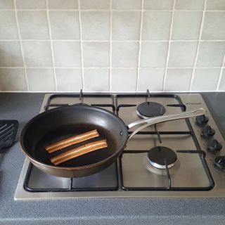 A frying pan holding two rashers of plant-based bacon on a stainless steel gas hob