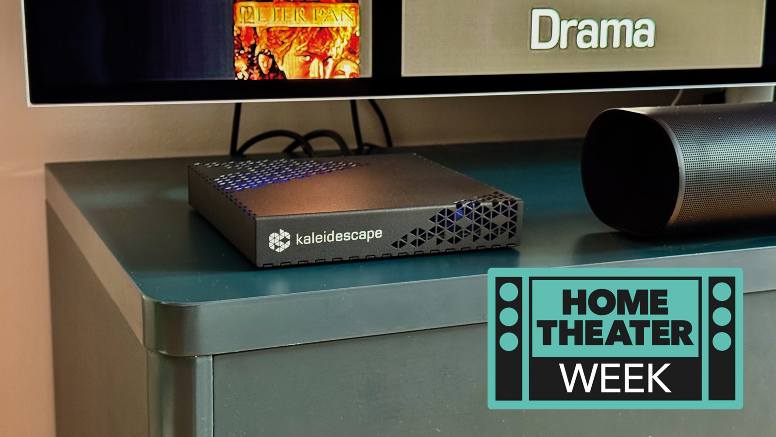 The Kaleidescape Strato E Movie Player on a navy blue TV unit. A badge saying "Home Theater Week" is in the bottom right corner.