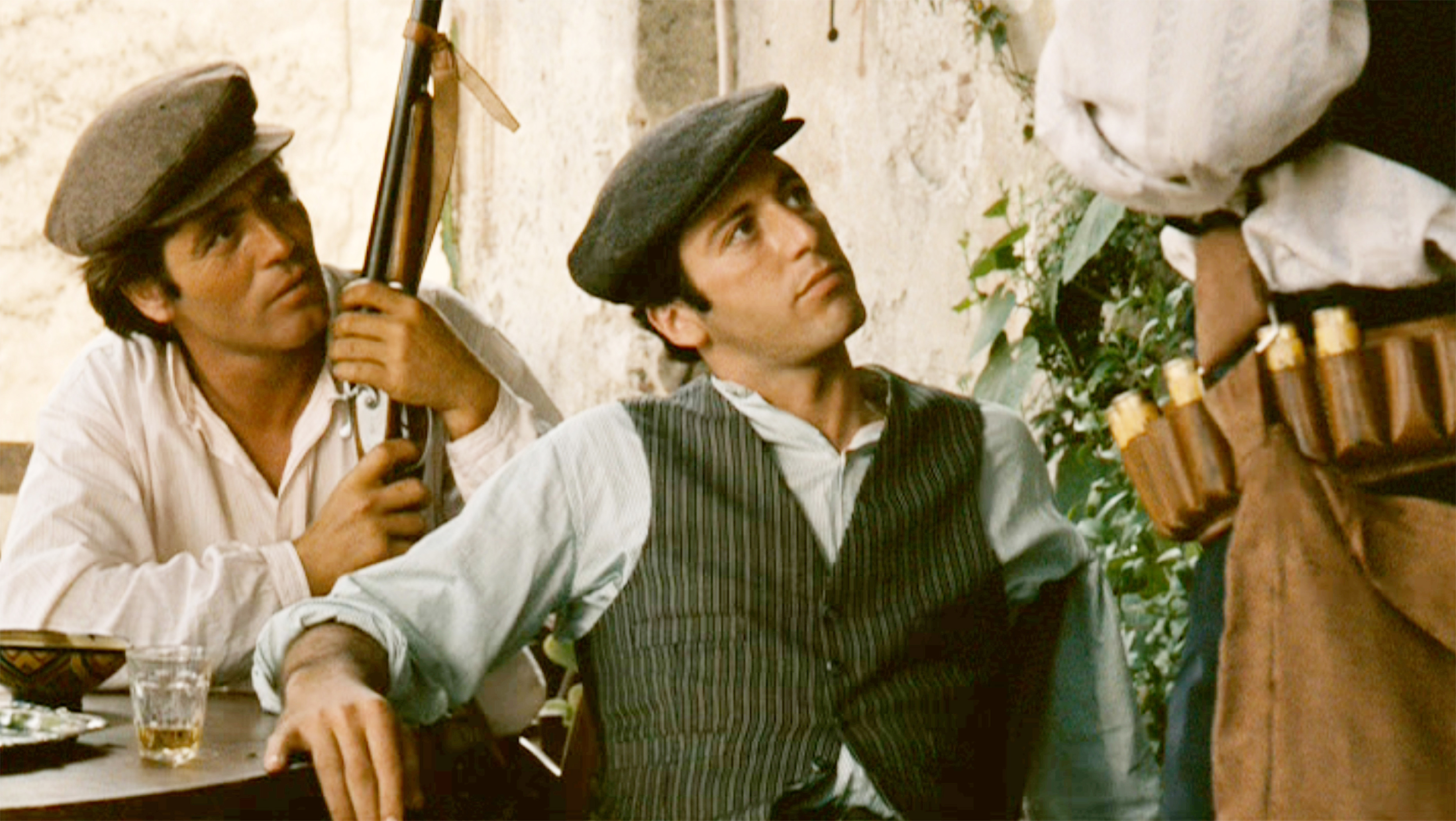 Al Pacino wearing a flatcap and waistcoat in 'The Godfather', next to an unnamed actor brandishing a rifle