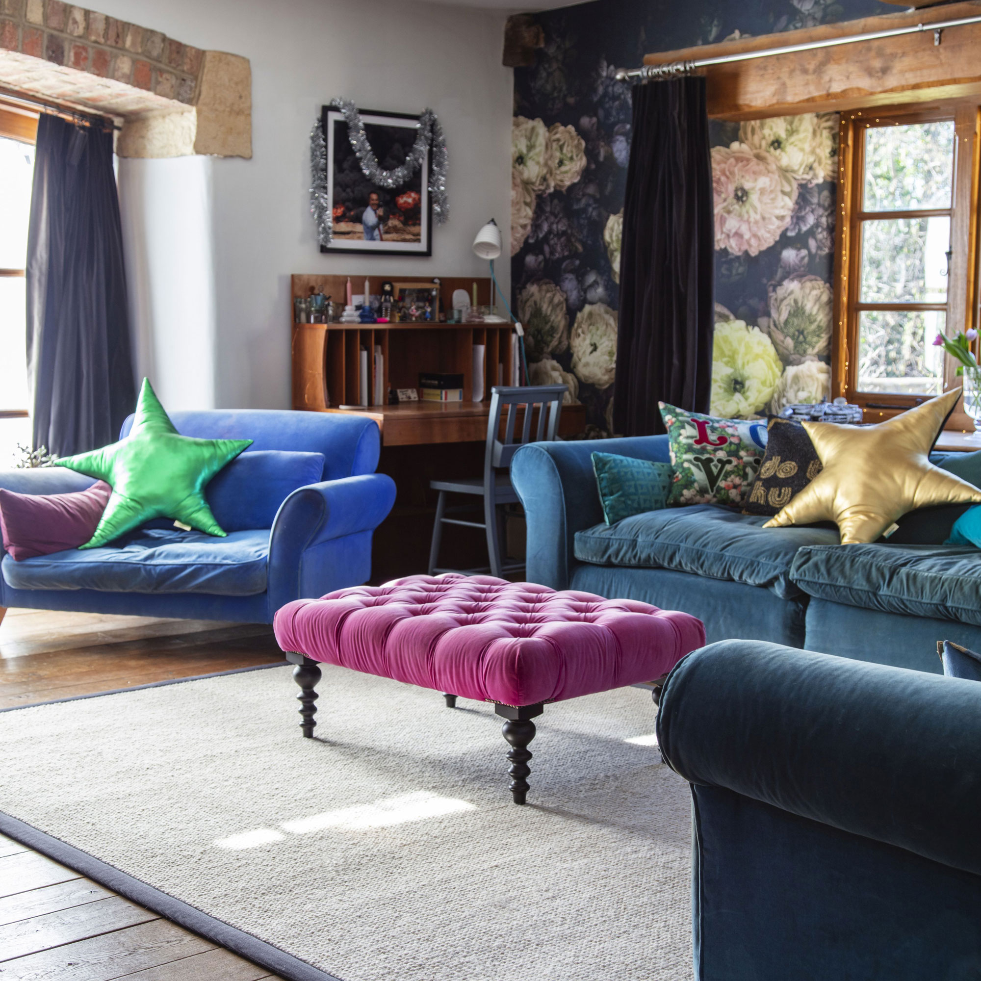 living room with blue velvet sofas and pink foot stool with cream rug and wooden flooring