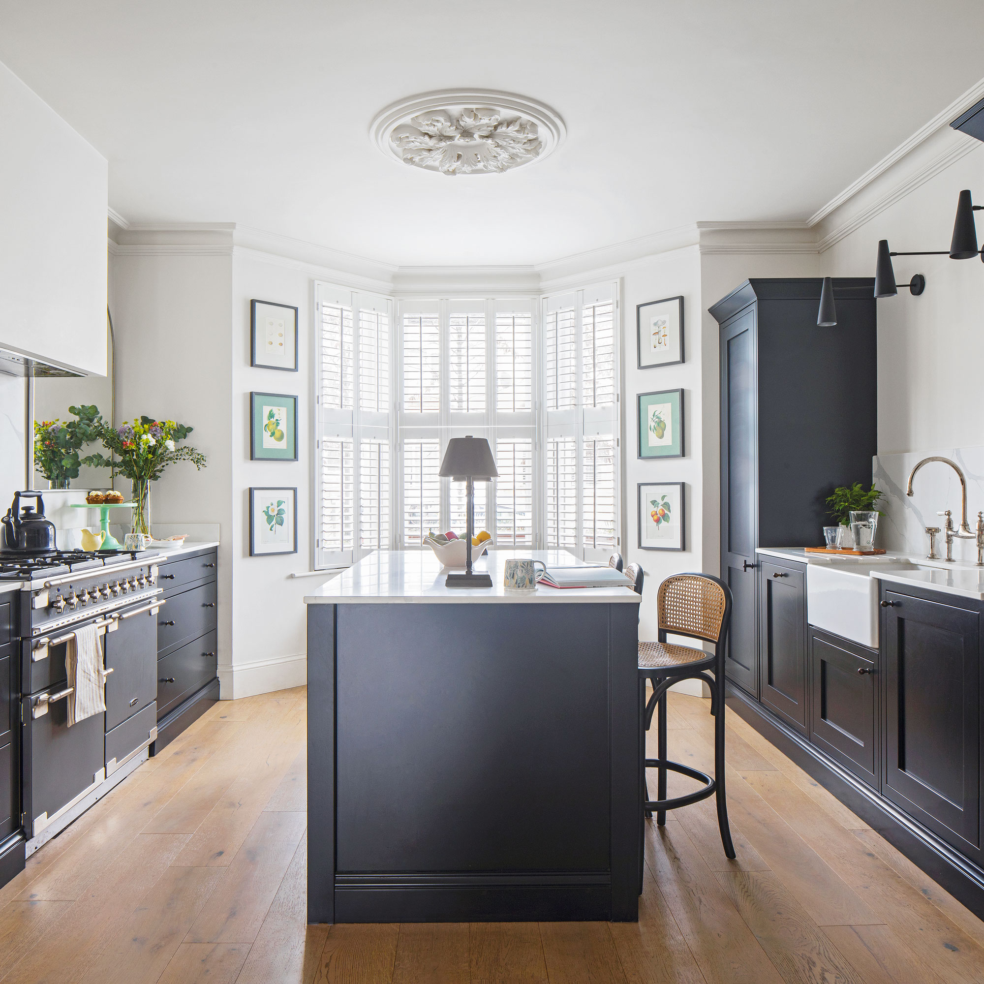 White kitchen walls with navy blue cabinets and a large bay window behind a kitchen island