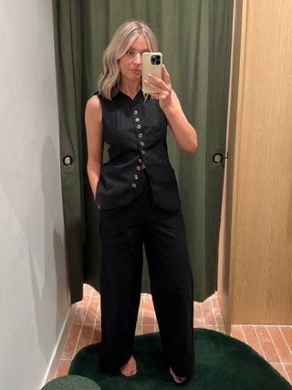 Woman in dressing room wears black waistcoat and black trousers