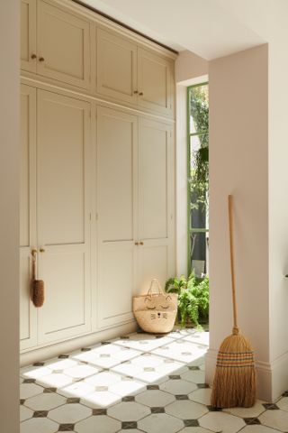 A mudroom with floor to ceiling cream cupboards and dusky pink walls