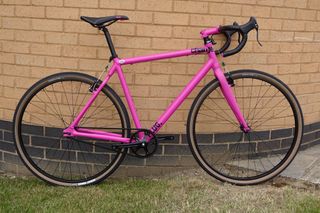 Charge Plug single speed is pictured in this image side on leaning up against a brick wall with the handle bars to the right.