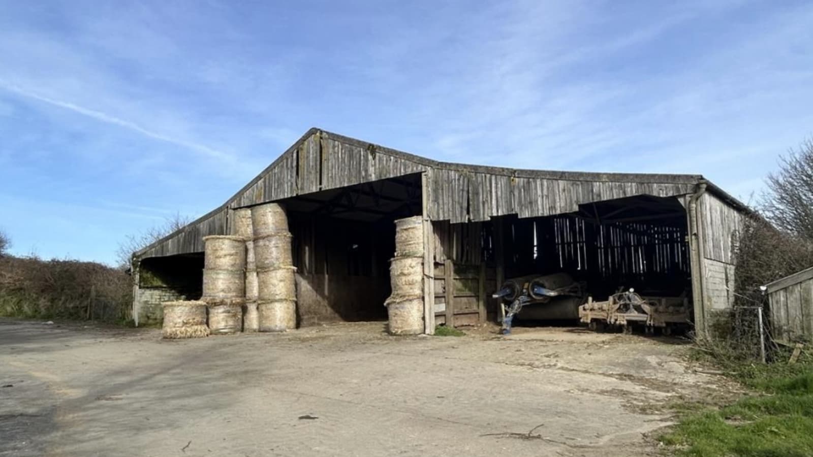 A barn with hay inside with a paved driveway